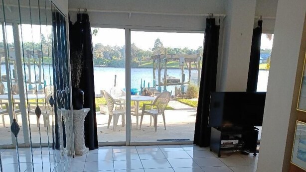 Quarto com uma cama grande, televisão e varanda com vista para um lago e móveis de exterior.
