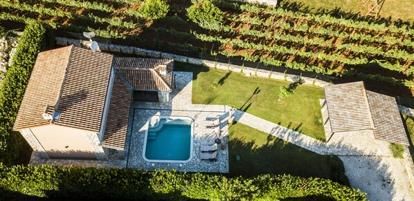 An aerial view of a property with a swimming pool, a tennis court, and a vineyard.