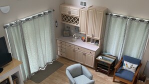 A compact living space with a kitchenette, two patterned armchairs, a wooden coffee table, and a sofa.