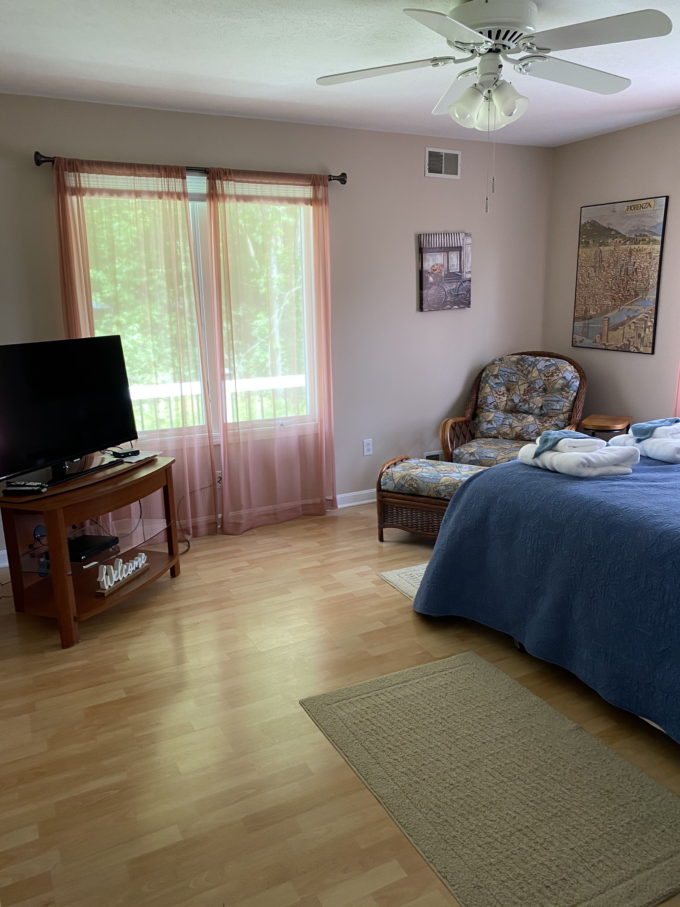 Une chambre à coucher avec un lit, une chaise, un téléviseur posé sur un meuble et un ventilateur de plafond.