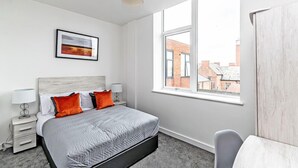 Une chambre moderne avec un grand lit, deux tables de chevet, une fenêtre donnant sur des immeubles et un tableau encadré au mur.