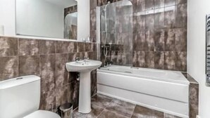 Une salle de bain moderne avec une baignoire, un lavabo sur colonne et un grand miroir.