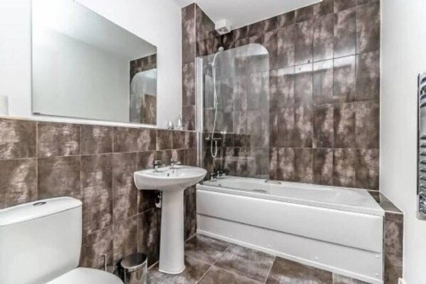 A modern bathroom with a bathtub, a pedestal sink, and a large mirror. - City Suites by Guestz (Chester)