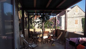 An outdoor patio with a table and chairs, surrounded by stone walls and flowering plants. - Mala Kapela is an authentic family home (Vrboska)