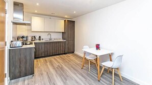Una cocina compacta con comedor, que incluye una mesa y sillas blancas, estufa integrada y suelo de madera.