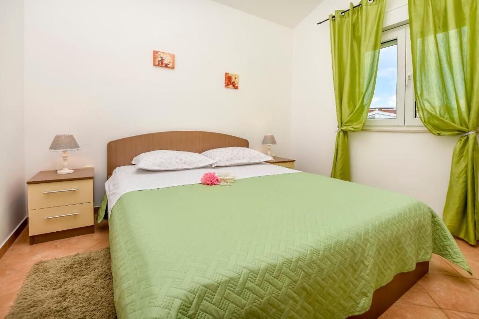 A bedroom with a bed, two bedside tables, a green curtain, and a window.