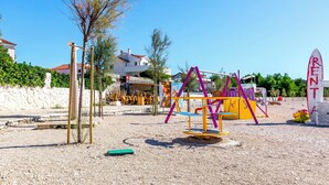 Ein Spielplatz mit Schaukeln und einer Rutsche, ein weißes Gebäude mit rotem Dach und ein Schild mit der Aufschrift 'RENTAL'.