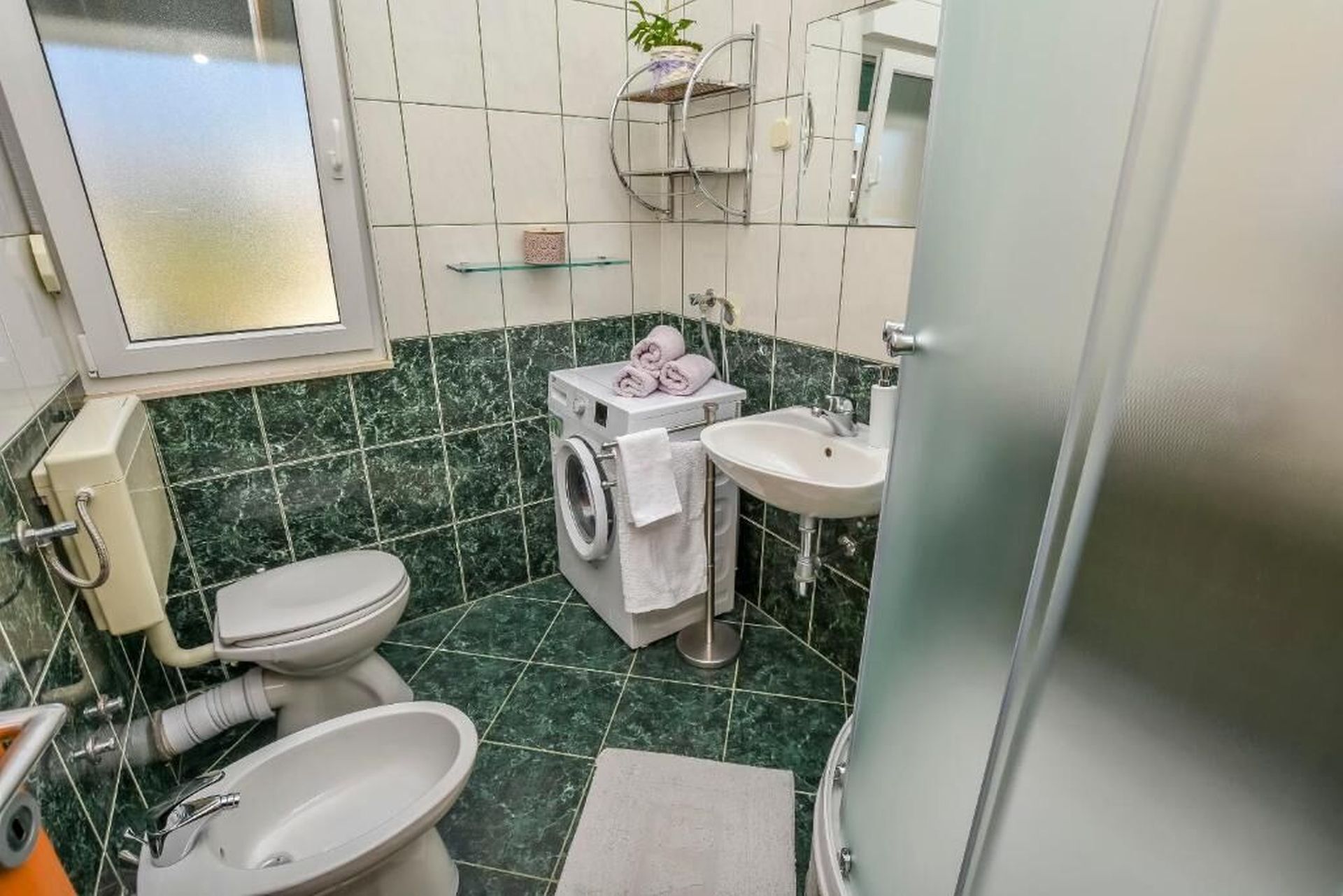 Ein kleines Badezimmer mit Toilette, Waschmaschine, Waschbecken und einem kleinen Fenster.