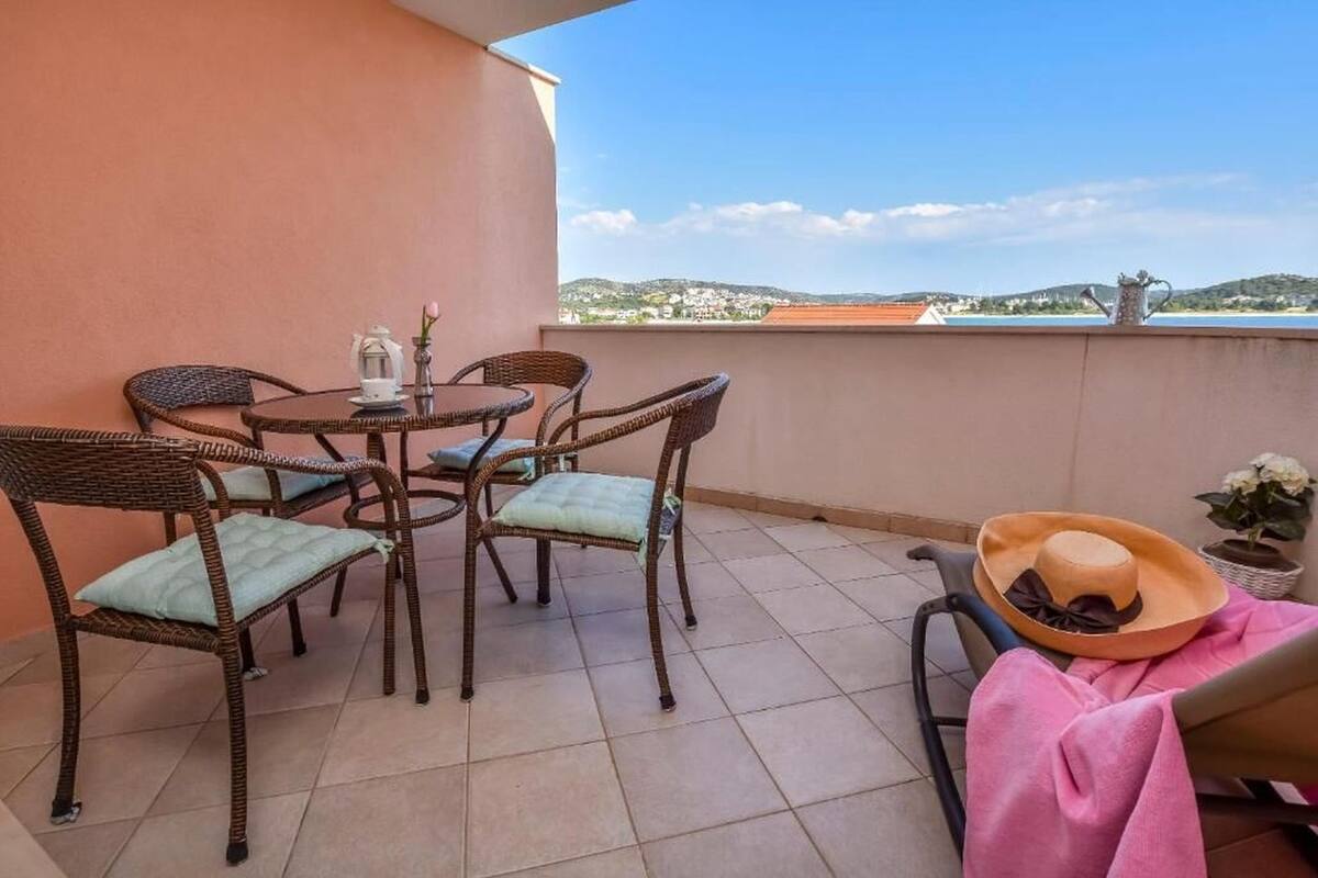 Un balcón con mobiliario de mimbre, una mesa y una planta en maceta.