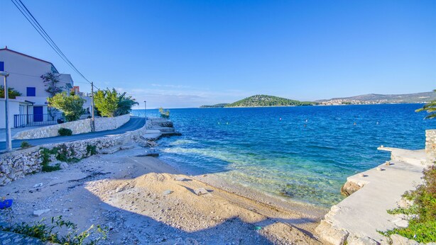 A coastal scene with a clear blue sea, rocky shoreline, and a building with a balcony. - Apartment Mezaroca (Razanj)