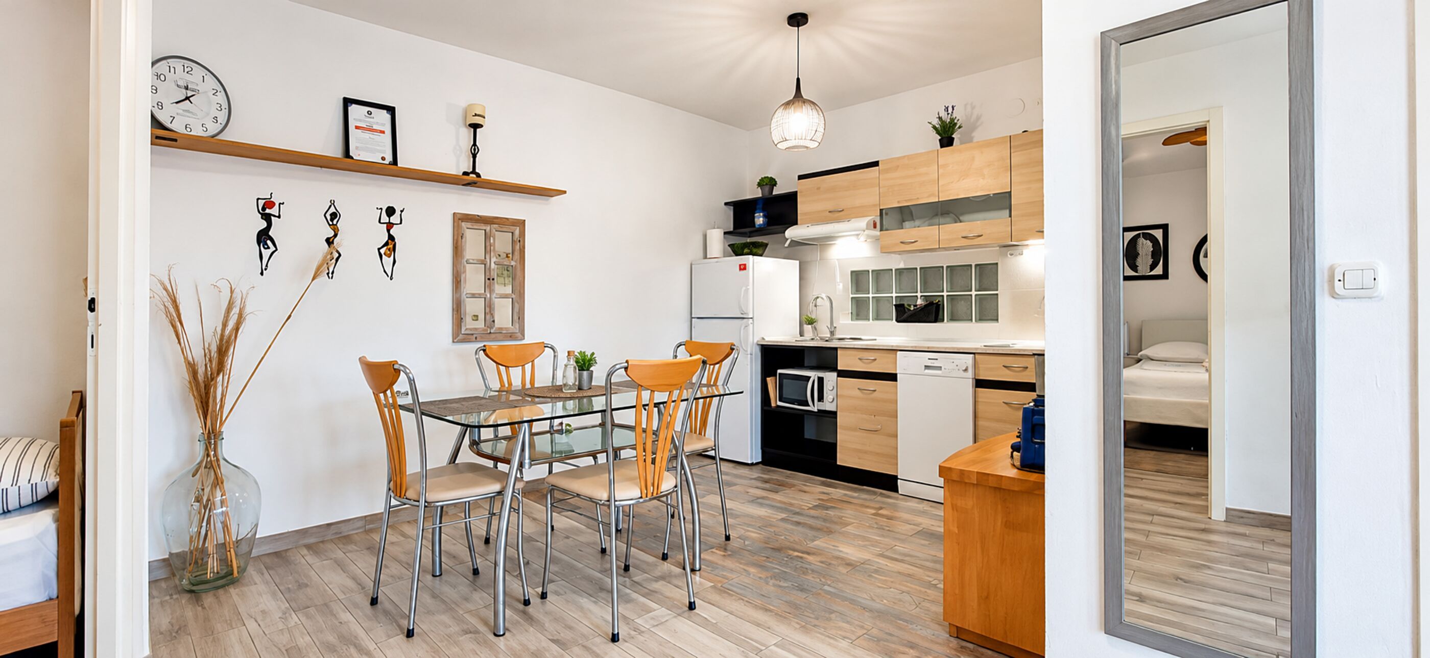 Une cuisine moderne avec des meubles en bois, un réfrigérateur blanc et un coin repas comprenant une table en verre et des chaises en métal.