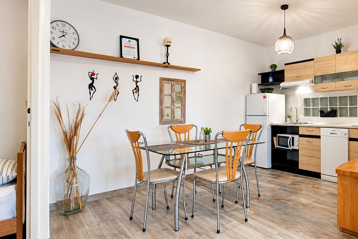 A modern kitchen with wooden cabinets, a white refrigerator, and a dining area with a glass table and metal chairs.