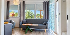 Un salon moderne avec un canapé gris, une table basse en bois et une vue sur la verdure à l’extérieur.