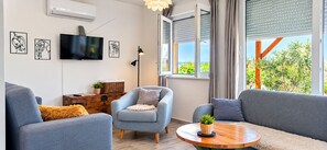 Ein modernes Wohnzimmer mit Flachbildfernseher, Kunstwerken, einer Couch, einem Sessel und einem Tisch mit einer Pflanze.