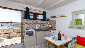A compact kitchen with a stone wall, a tiled backsplash, and a window with curtains. - Apartment Mezaroca (Razanj)