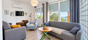 Un salon moderne avec un canapé gris, un fauteuil bleu, une table basse en bois et un téléviseur fixé au mur.