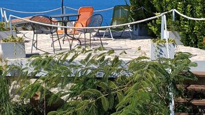 An outdoor seating area with a table, chairs, and an umbrella overlooking a coastal view. - Apartment Mezaroca (Razanj)