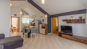 A modern living room with a sofa, a dining area with a table and chairs, a kitchen in the background, and a TV on a wooden stand. - Apartments Grgo (Vodice)