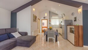 A modern living room with a sofa, a dining table with chairs, a kitchen area with a refrigerator, and a hallway leading to another room. - Apartments Grgo (Vodice)