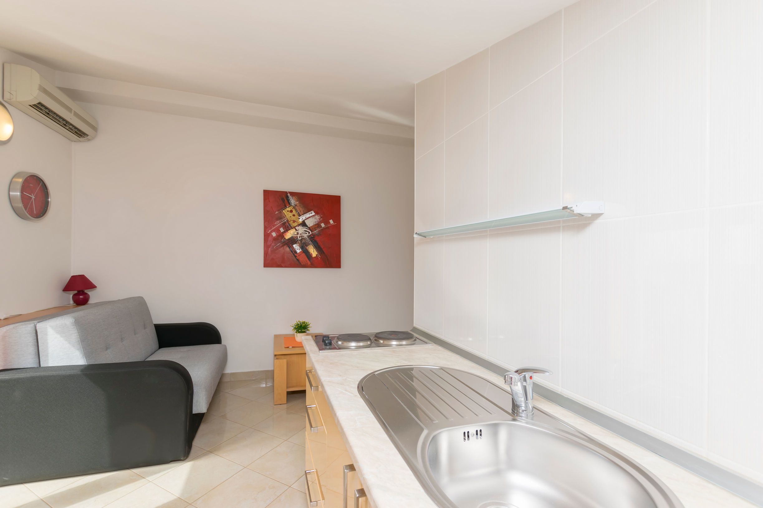 Una cuina moderna amb un sofà gris, un rellotge vermell i un quadre a la paret.