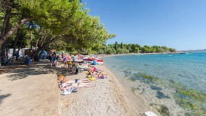 Una spiaggia con acqua cristallina, persone che prendono il sole e alberi.