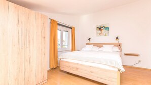 Una camera da letto con un letto in legno, un armadio, una finestra con tende e un quadro appeso al muro.