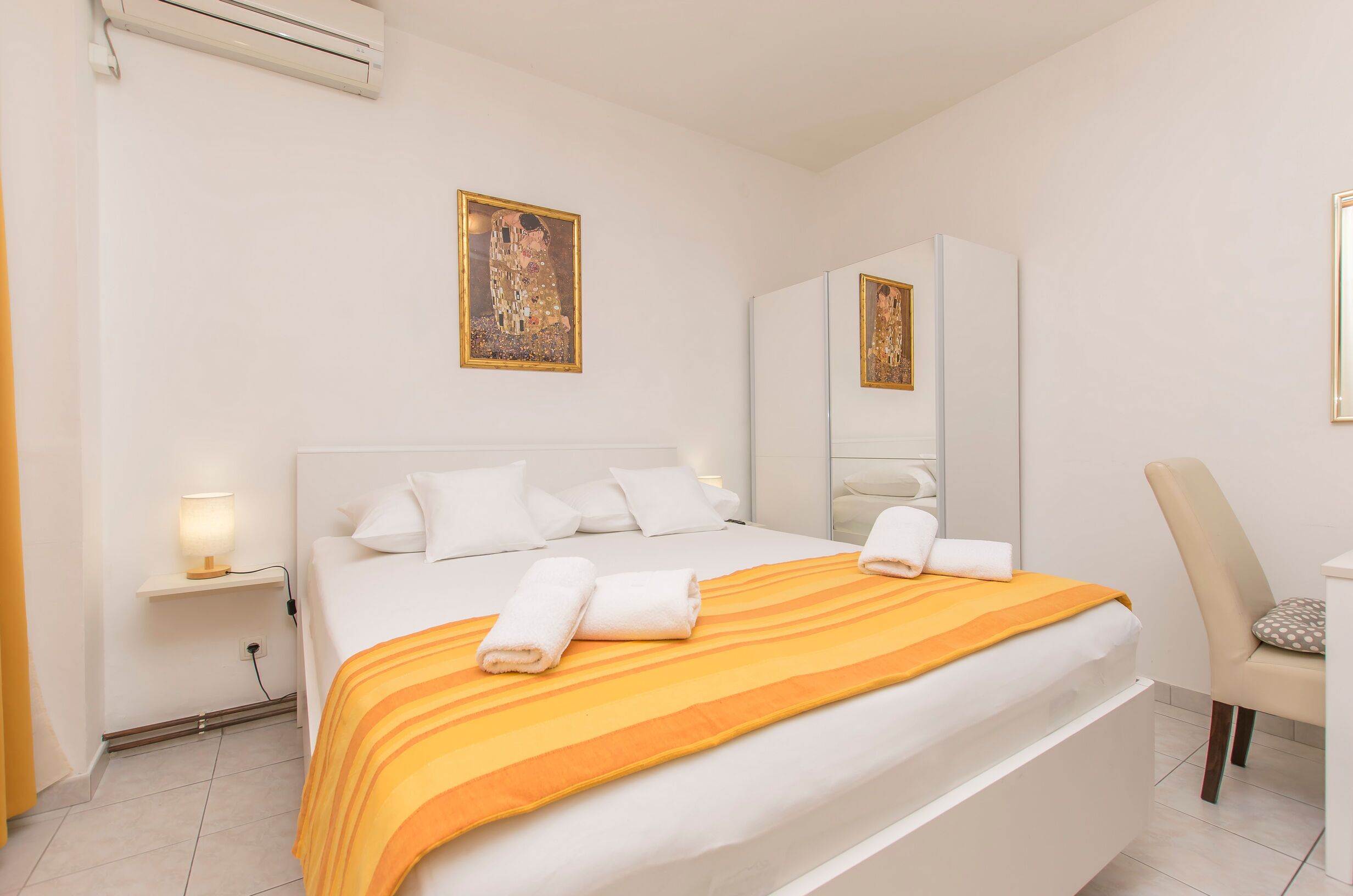A hotel room with a large bed, a bedside table with a lamp, a chair, and a mirror.