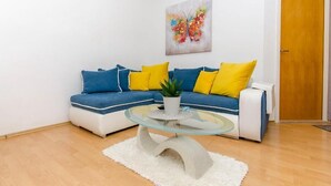 A modern living room with a blue and white sofa, yellow cushions, a glass coffee table, and a white rug. - Apartments Otjana (Sevid)