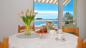 A table set for breakfast with a view of the sea, a vase of flowers, and a fruit bowl. - Apartments Sandy (Rogoznica)