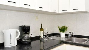 A kitchen with white cabinets, a coffee maker, a wine bottle, a glass, and a potted plant. - Apartments Sandy (Rogoznica)