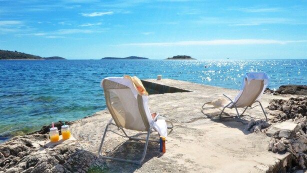 Two beach chairs on a rocky shore with a view of the sea and distant islands. - Apartments Sandy (Rogoznica)