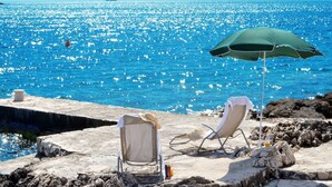 A beach with two sun loungers and a green umbrella, overlooking a sparkling blue sea. - Apartments Sandy (Rogoznica)