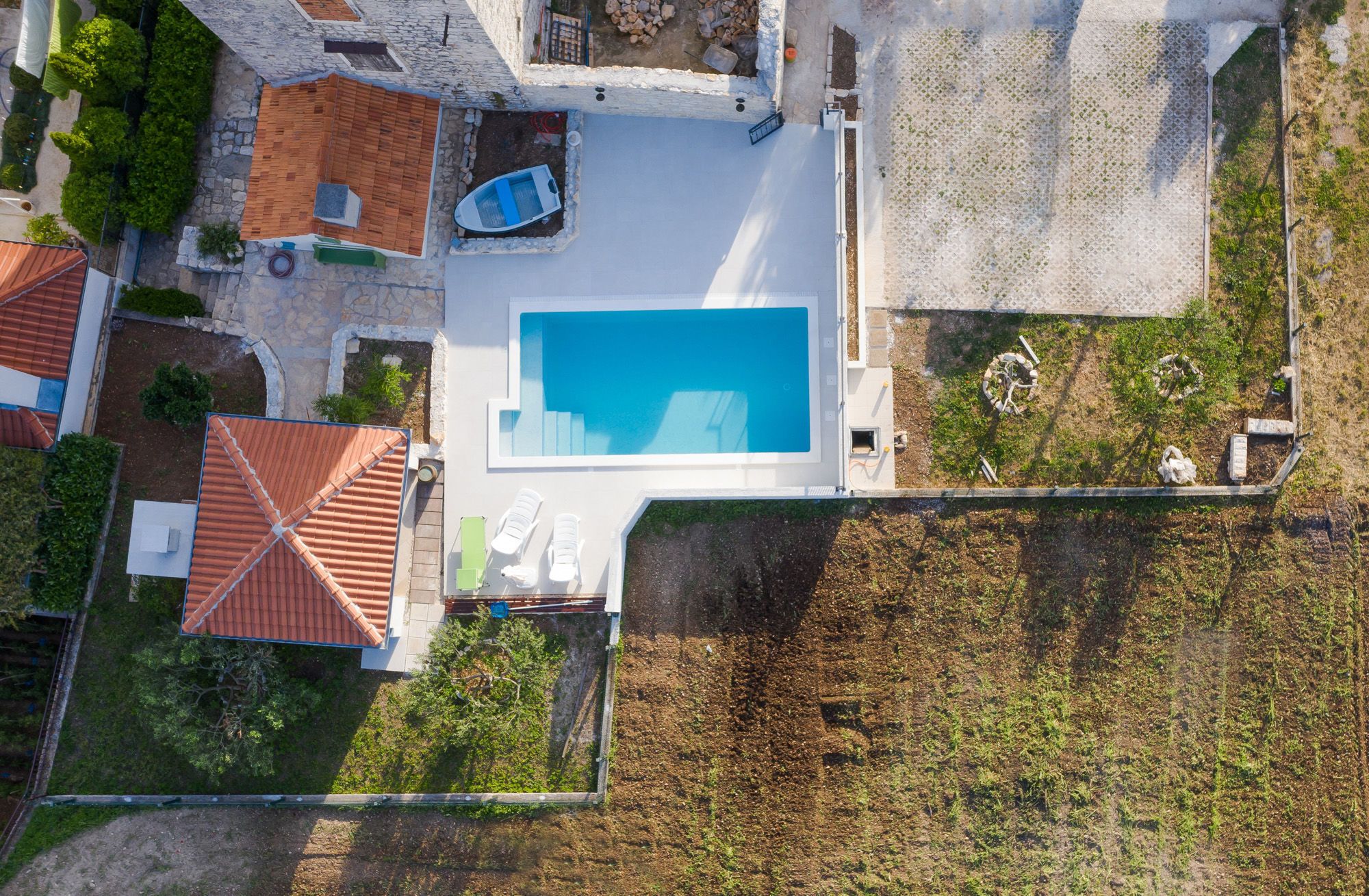 Eine Luftaufnahme eines Anwesens mit Swimmingpool, Kleinboot und einem eingezäunten Garten.