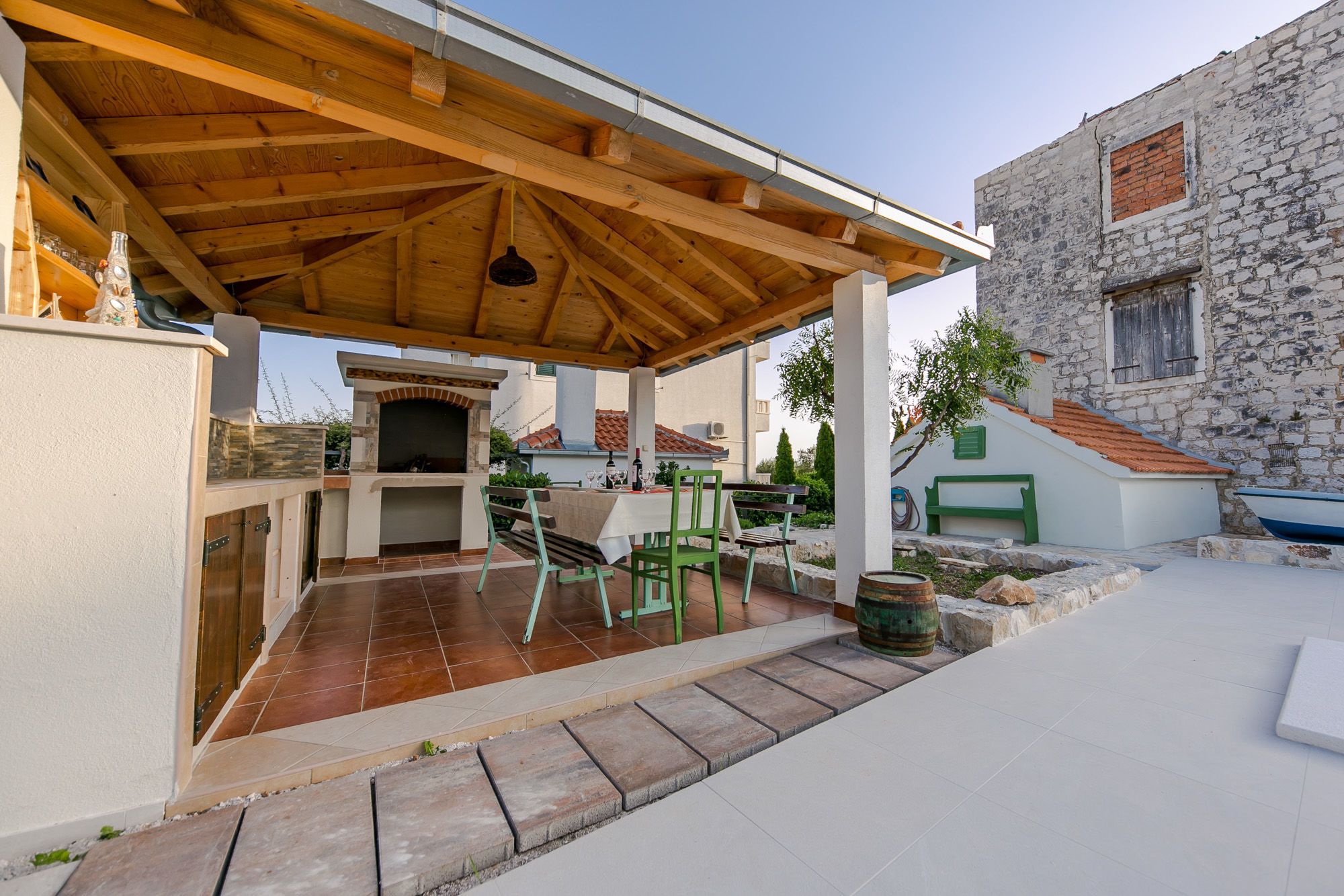 Une terrasse extérieure dotée d’une pergola en bois, d’un barbecue et, au fond, d’un bâtiment en pierre.