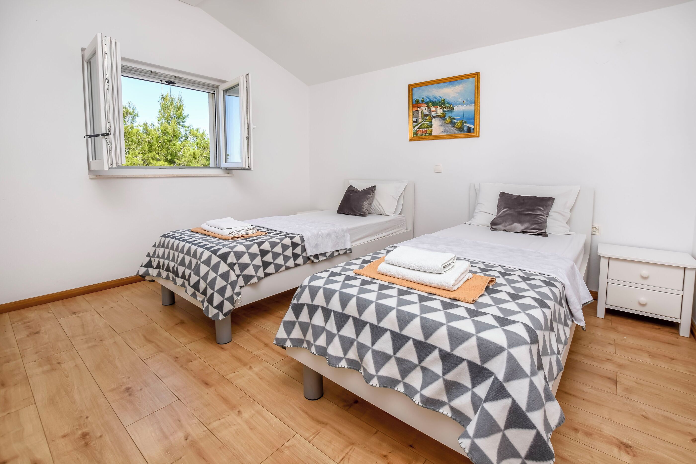 A bedroom with two beds, a window, a painting, and a nightstand.
