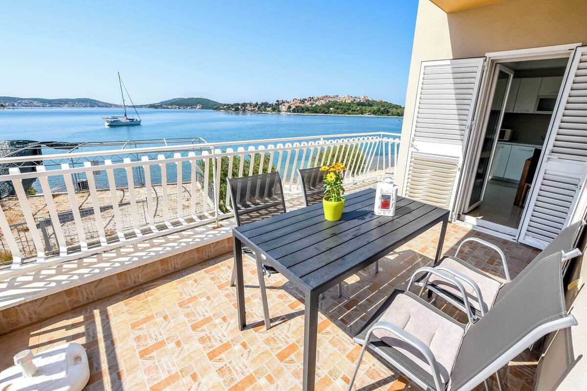 Un balcon avec une table, des chaises et un pot de fleurs.