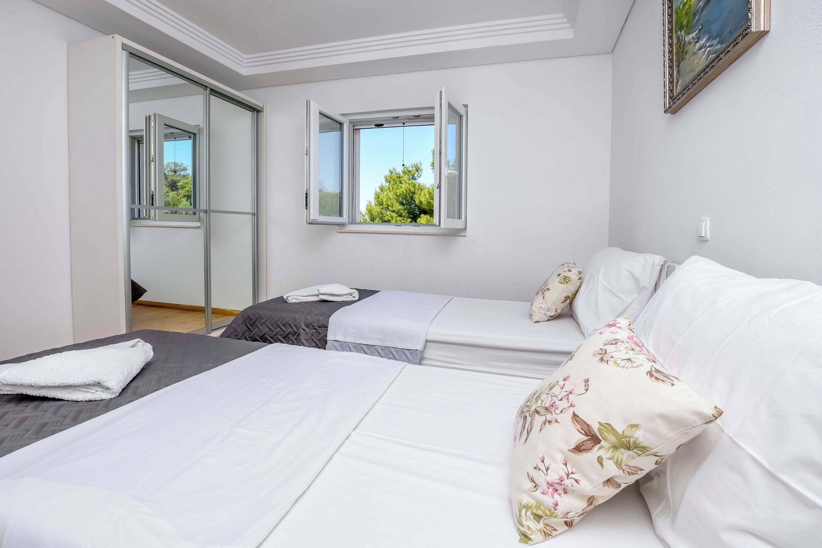 Habitación de hotel con dos camas, un espejo grande y dos ventanas con contraventanas abiertas.