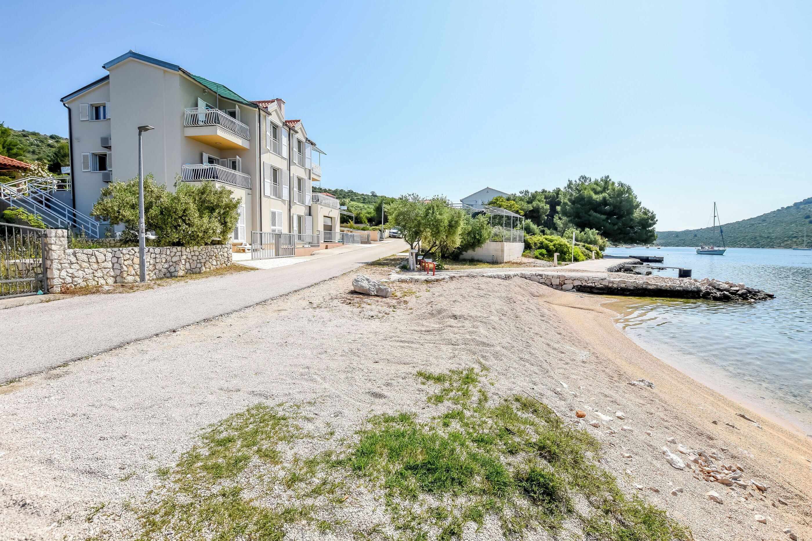 A coastal building with balconies, a sandy beach, and a calm sea.