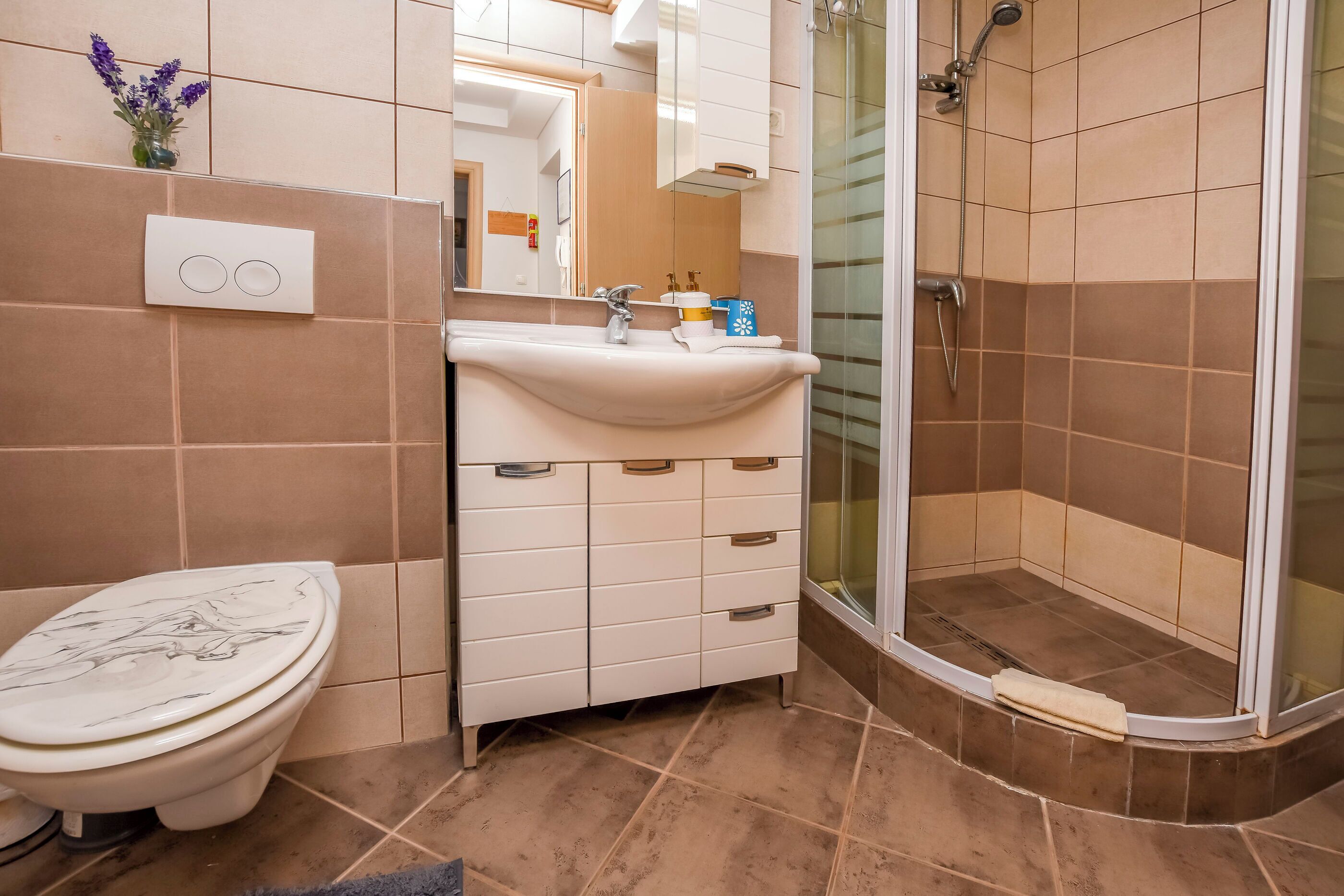 A bathroom with a toilet, sink, mirror, and shower.