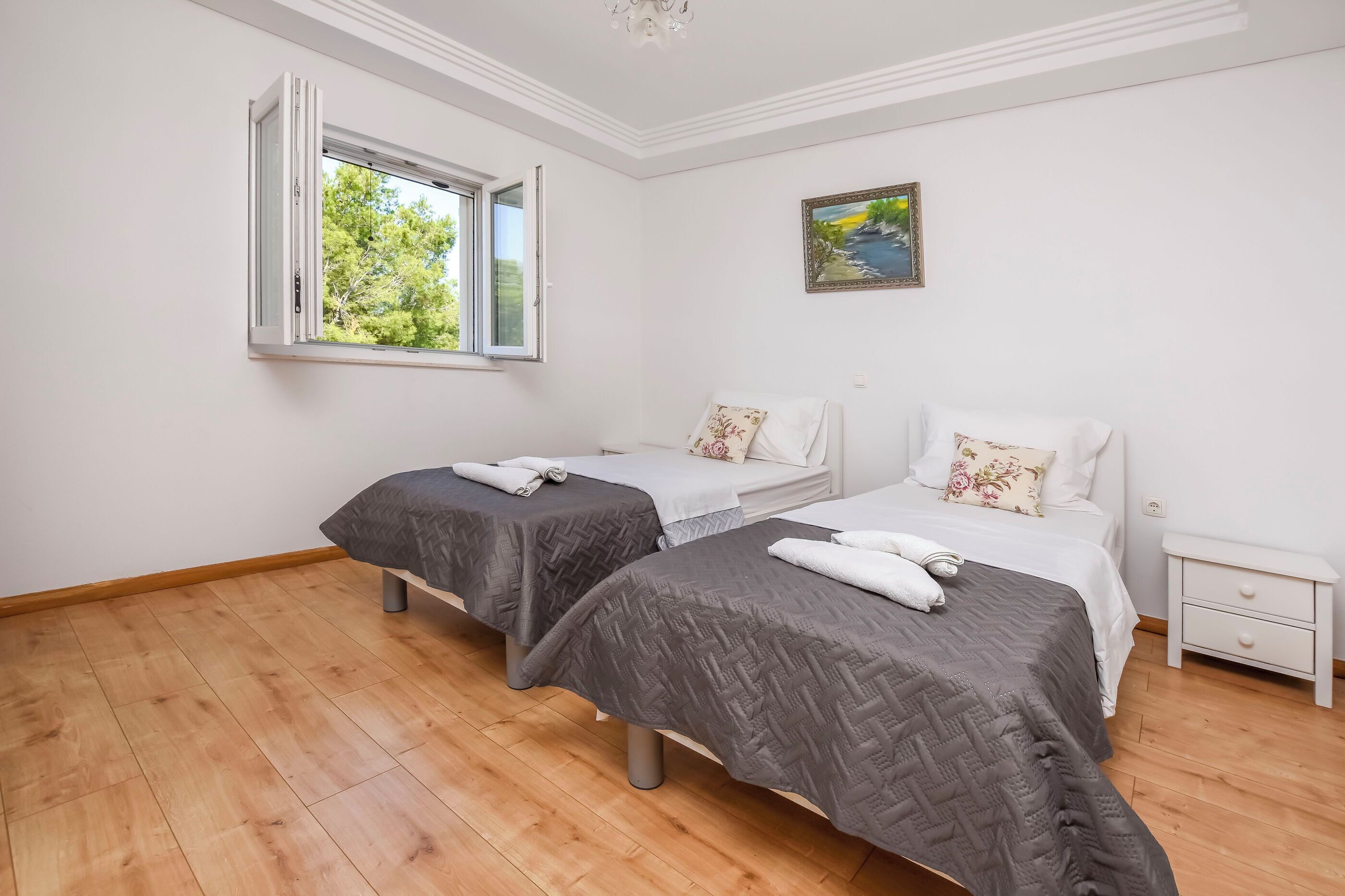 A room with two beds, a window, a painting, and a nightstand.