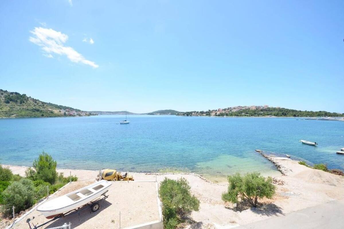 Une vue sur la côte, avec un bateau amarré sur une plage de sable, une mer bleue et limpide, et des collines à l’horizon.
