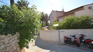 Una calle estrecha con un muro de piedra, un cartel de restaurante y dos scooters estacionados.
