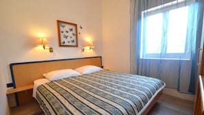 Habitación de hotel con cama, dos lámparas adosadas a la pared, una obra de arte con mariposas en marco y una ventana con cortinas.