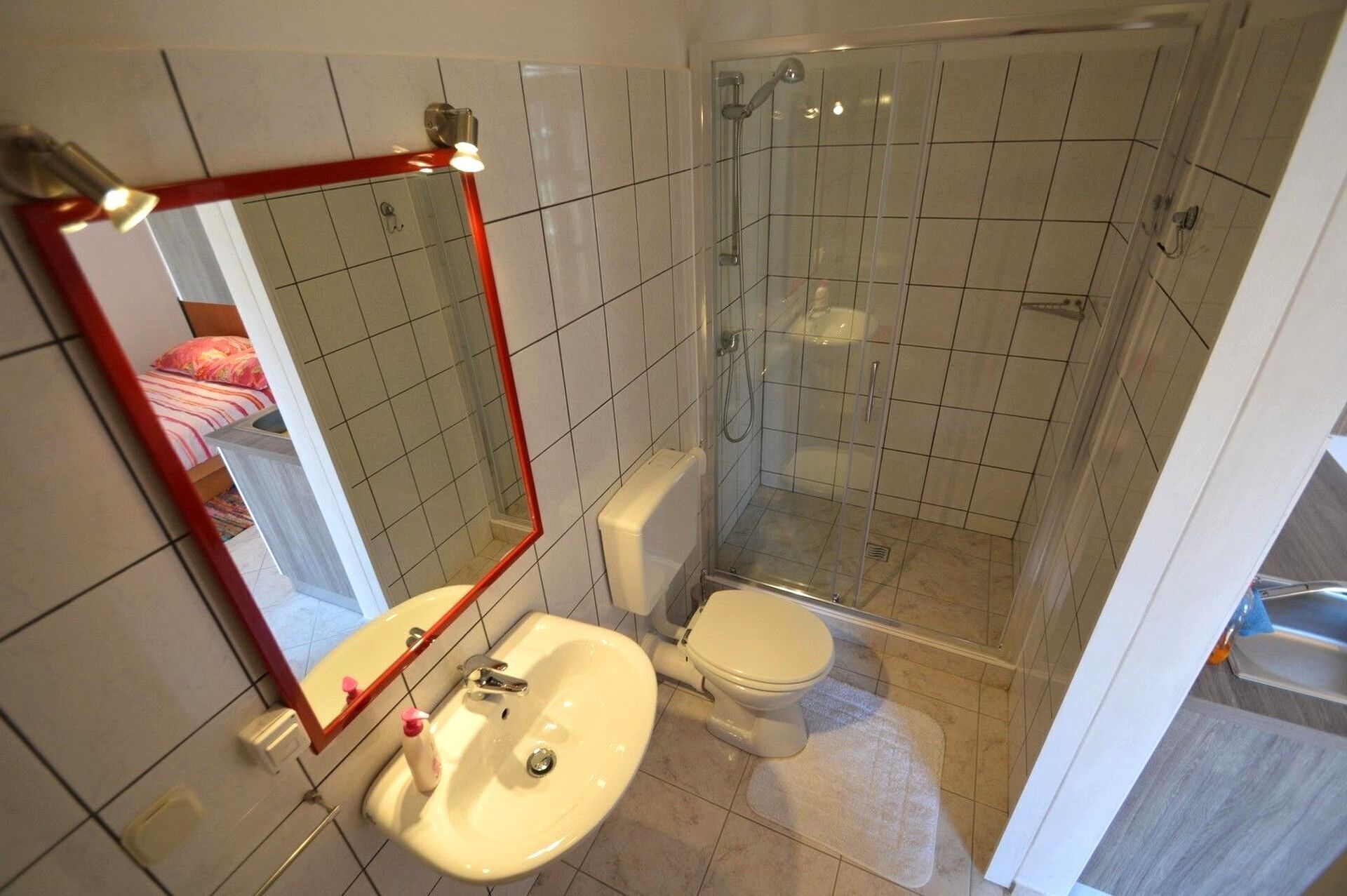 A bathroom with a toilet, sink, shower, and a mirror.