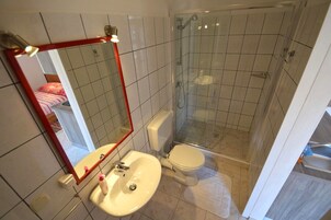 Baño con inodoro, lavamanos, ducha y espejo.