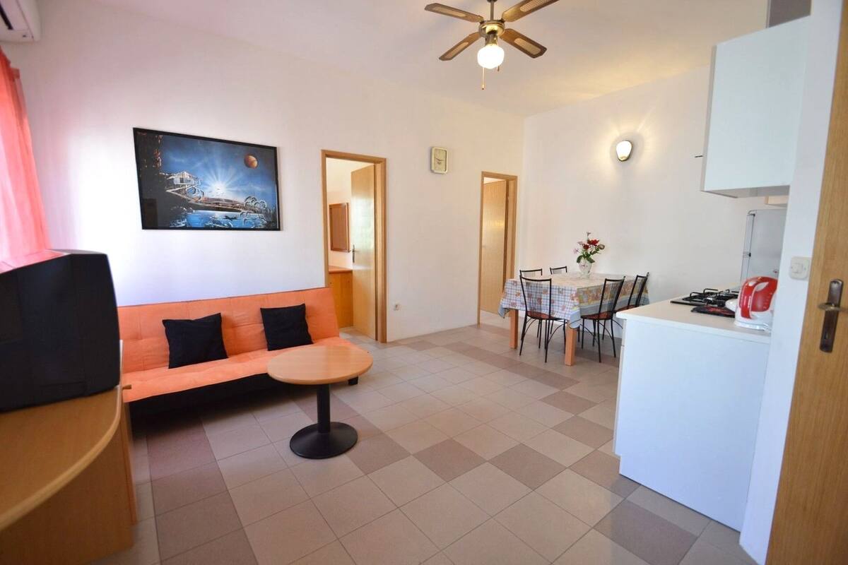 Un espace de vie compact comprenant un canapé, une petite table ronde, une table à manger avec des chaises, un coin cuisine avec une cuisinière et un ventilateur de plafond.