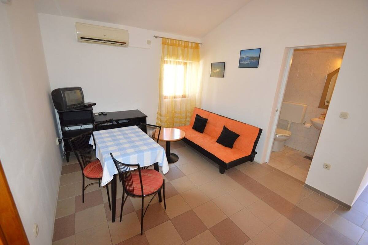 Un espace de vie compact comprenant un coin repas, un canapé, un téléviseur et une petite kitchenette.