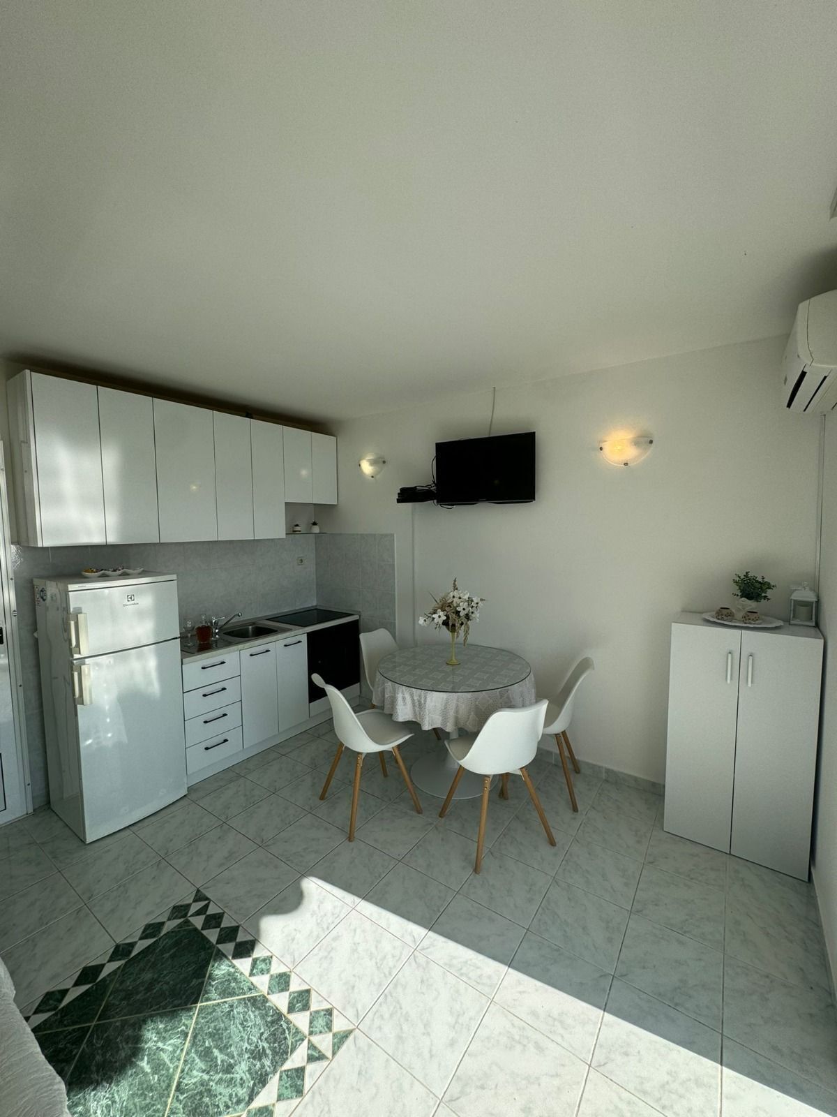 Una cocina compacta con armarios blancos, horno empotrado y comedor con una mesa redonda y sillas.