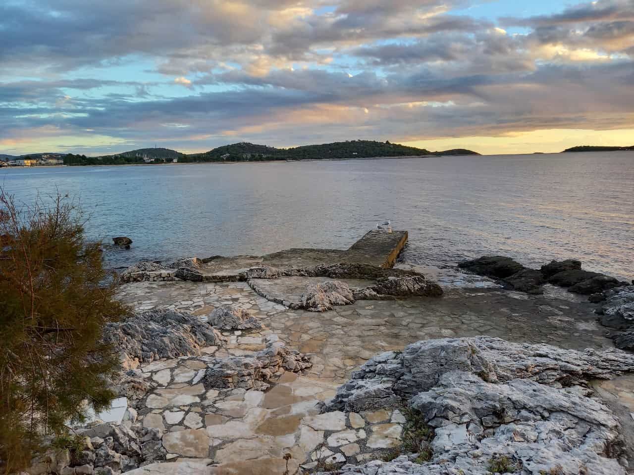 A rocky shoreline with a calm body of water and distant hills.