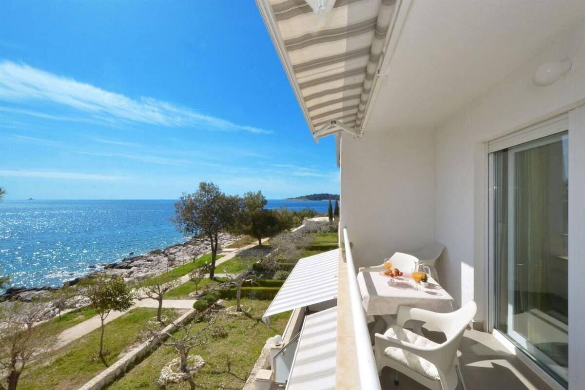 Un balcon avec une table et des chaises, offrant une vue sur la côte et un ciel dégagé.